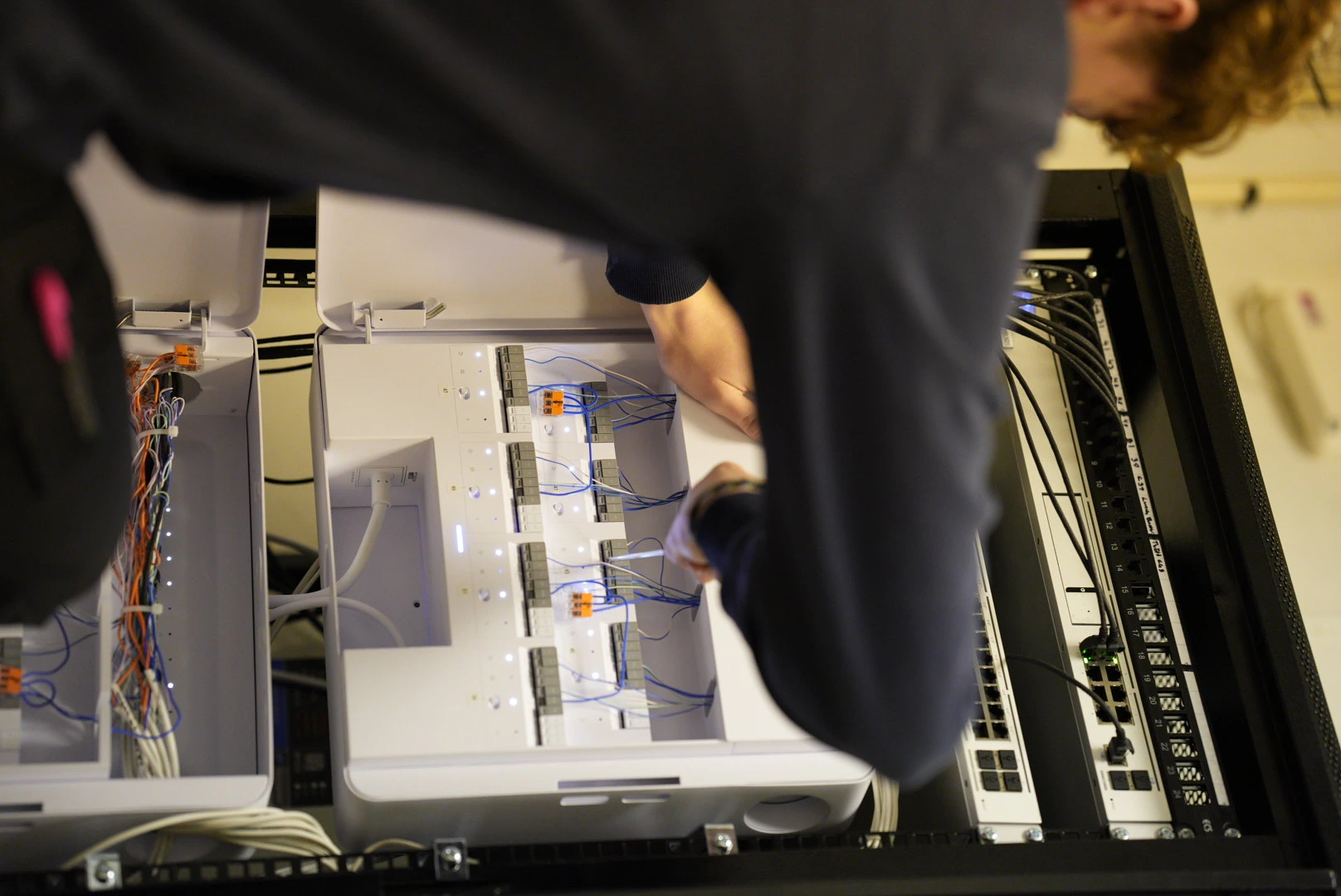 Elektriker granskar ritningar i industrilokal med verktyg och kablar på golvet.